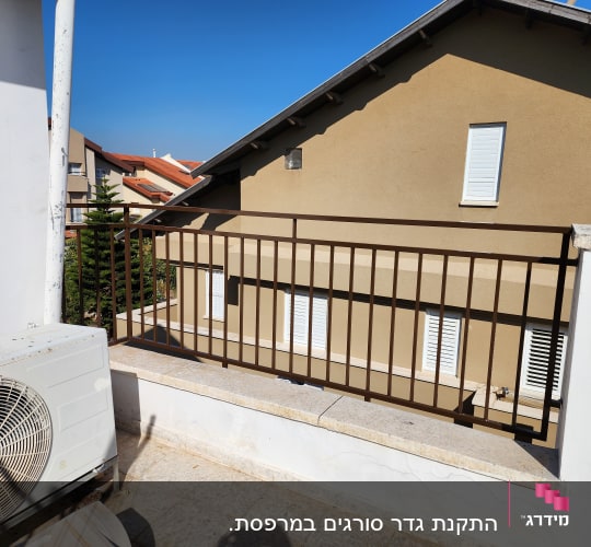 מעקה מתכת חום על מרפסת עם קיר לבן
